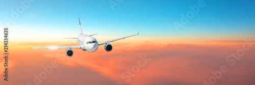 Passenger aircraft cloudscape with white airplane is flying in the orange sky with colorful sunset, panorama view.