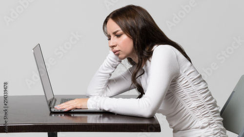Incorrect, impaired posture position, defect scoliosis, orthopedics concept.  Young woman sitting at table, looking and working at laptop, isolated. Rachiocampsis. Kyphosis curvature of the spine