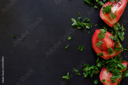 Tomatoes with parsley on a black wooden board. Cut red tomato with greens on a black background. Summer  refreshing background for detox programs  diets  fruitarians. Menu page for salads. Empty place