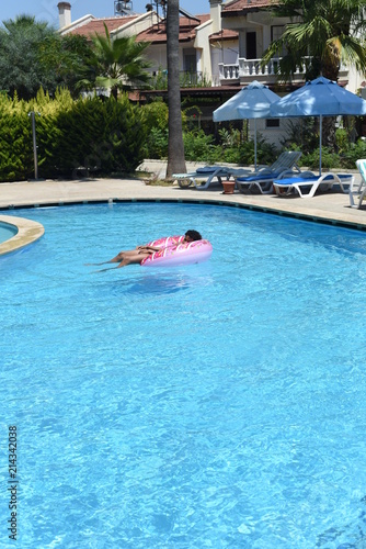 Happy cute little african-american boy lying on an inflatable donut circle  in the swimming pool in the hotel. Cool summer holidays for children and kids. Active games on the water.  Pink donat. 