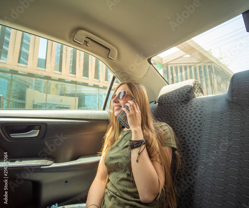 A young girl is sitting in the back seat of a car and is talking on the phone. photo