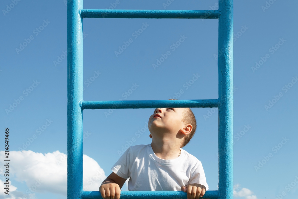 Fototapeta premium The blond boy climbs the stairs on the playground and looks up.