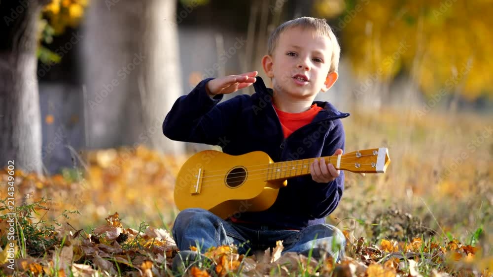 Portrait of funny child sing at guitar, happy kid clapping his hands in park Portrait of funny child sing at guitar, happy kid clapping his hands in park