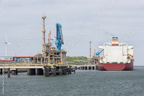 Liquid gas transshipment terminal in harbor Rotterdam, biggest seaport of Europe. In the background a freighter and a wind turbine.