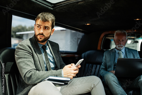 Senior businessman and his assistant sitting in limousine and working together.