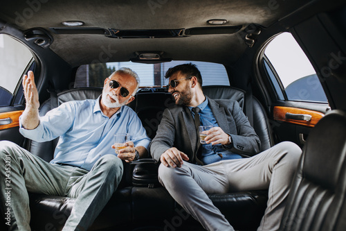 Fototapeta Senior businessman and his assistant sitting in limousine and celebrating their job success