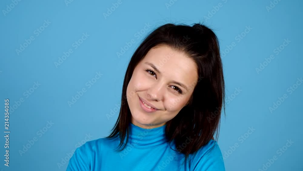 Close up of beautiful woman smiling at the camera on blue background. Attractive happy girl portrait. Slow motion footage Close up of beautiful woman smiling at the camera on blue background. Attractive happy girl portrait. Slow motion footage
