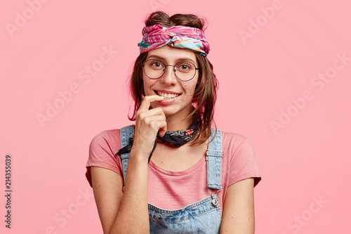 People, subculture and freedom concept. Delighted satisfied hippie woman with gentle smile, meets with friend, have pleasant talk, wears stylish bandana on head, isolated over pink background
