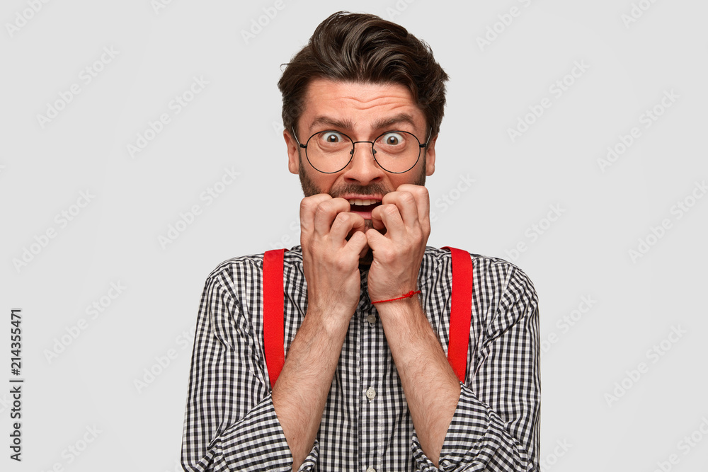 Nervous bearded male bites finger nails and looks anxiously, has puzzled expression, afraids of something, wears stylish clothes. People, youth, fear and confusement concept. Stressed hipster Nervous bearded male bites finger nails and looks anxiously, has puzzled expression, afraids of something, wears stylish clothes. People, youth, fear and confusement concept. Stressed hipster