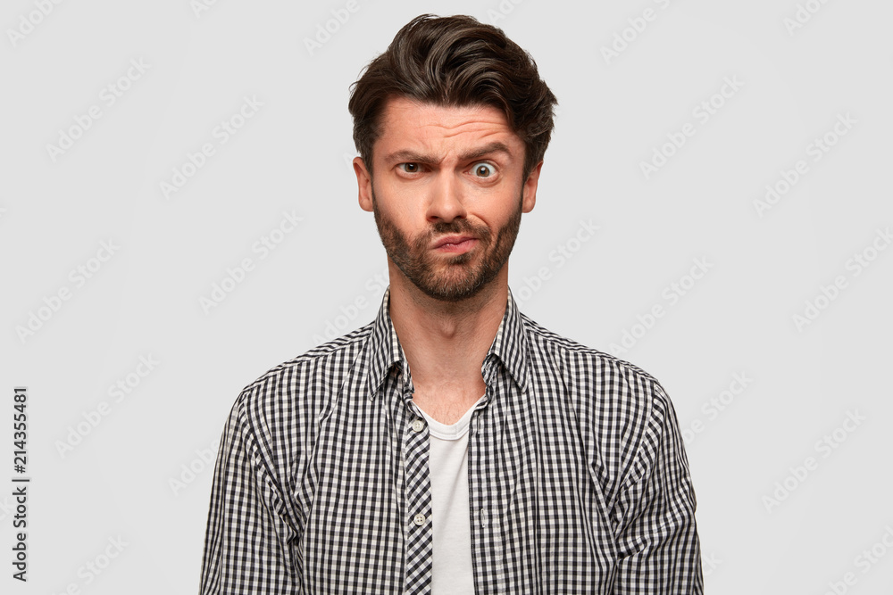 Displeased young male journalist frowns face, has puzzled expression, discontent after making interview, has not much information for writing complete article, wears checkered shirt has trendy haircut Displeased young male journalist frowns face, has puzzled expression, discontent after making interview, has not much information for writing complete article, wears checkered shirt has trendy haircut