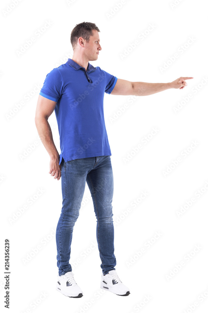Profile of young adult caucasian man in blue polo shirt pointing finger away showing copyspace. Full body isolated on white background. Profile of young adult caucasian man in blue polo shirt pointing finger away showing copyspace. Full body isolated on white background.