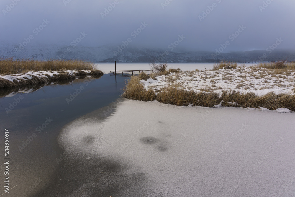 Scenic View Of Frozen Lake Against Foggy Mountains
