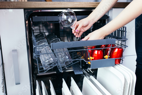 Close up shot of woman's hand taking out clean dishes from dishwasher machine.