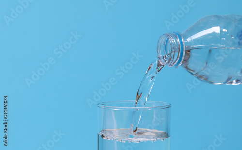 Pouring mineral drinking water from bottle into glass with blue background. 