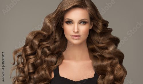 Brunette brown girl with long  and   shiny curly hair .  Beautiful  model woman  with curly hairstyle. Care , cosmetic and beauty 

