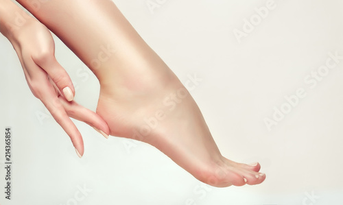 Perfect clean female feet . Beautiful and elegant groomed girl's hand touching  her foot  heel . Spa ,scrub and foot care .
