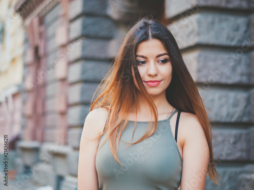 Portrait of young attractive girl with smile. Woman with oriental face, brown eyes and stylish ombre dyed long haistyle on architecture background. Street style.