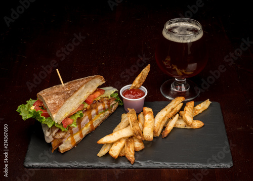 Fancy glass of beer with a half club sandwich with fries