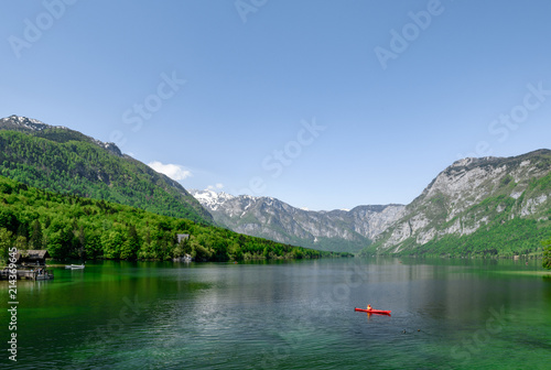 Concept picture of summer time at lake bohinj in Slovenia with red canoe in emerald color lake.