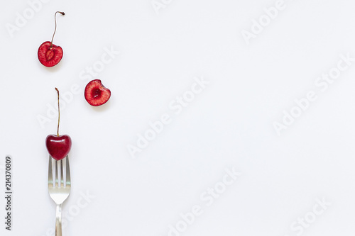 Red cherry fruits and fork on white background