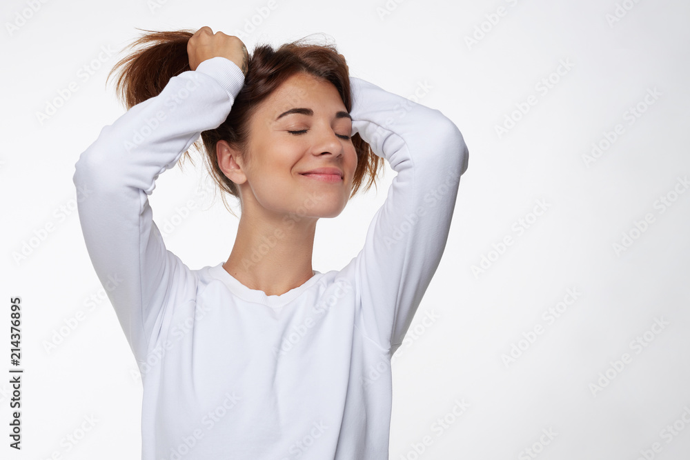 Delightful positive female expresses happiness, has broad charming smile, closes eyes from pleasure, laughs at funny joke, poses against white background with blank copy space for your advertisement. Delightful positive female expresses happiness, has broad charming smile, closes eyes from pleasure, laughs at funny joke, poses against white background with blank copy space for your advertisement.