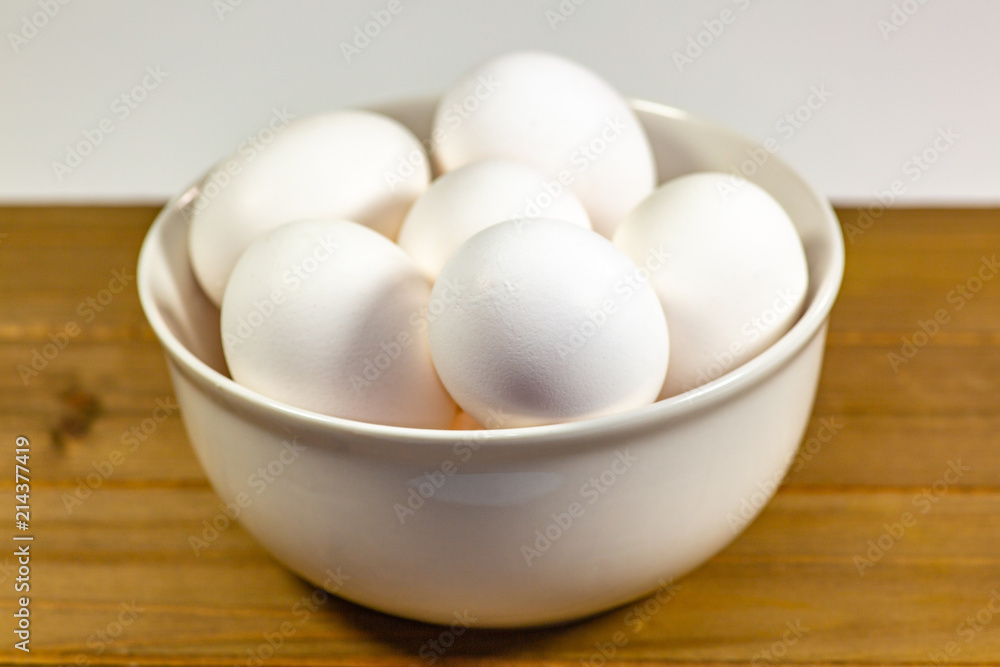 A group of eggs inside a deep white bowl next to a whisk waiting for the chef to use them in a meal