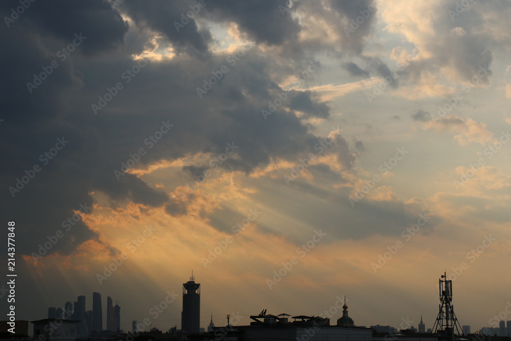 Romantic sunset and the setting sun on blue and yellow clouds above the roofs of buildings