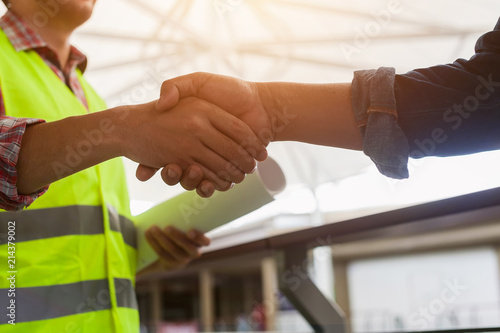 Construction workers in protective helmets and vests are shaking hands