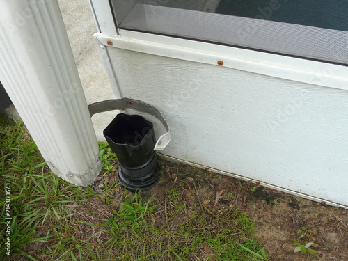 Installing Residential Downspout Connector DIY Project. A connector between the downspout and drainage pipe is being installed on a house to seal out debris and prevent foundation damage from water.