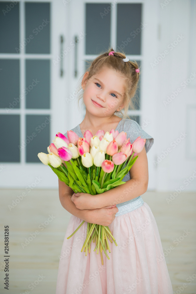 Adorable smiling little girl with tulips by the window Adorable smiling little girl with tulips by the window