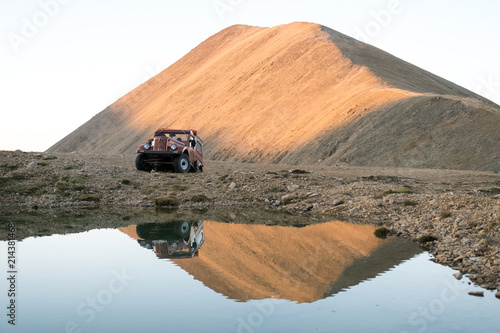 Старый внедорожник на берегу горного озера на фоне красной горы на закате
