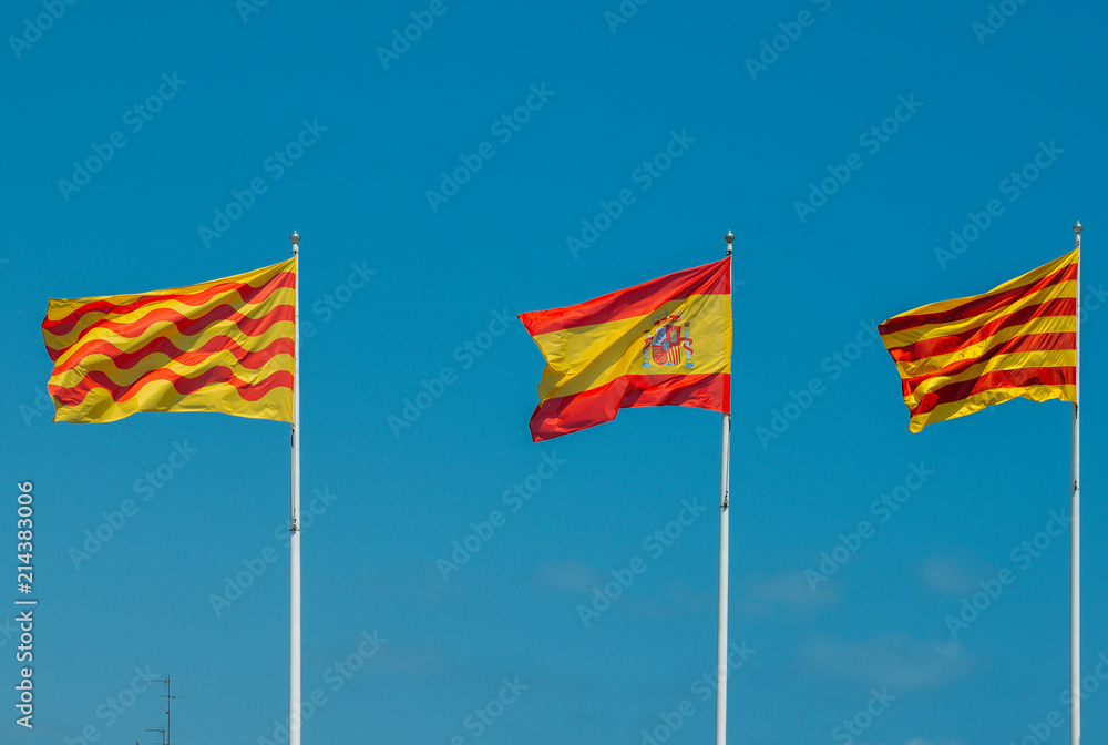 Catalonian, Spanish and Tarragonian flags flying on a mast against a blue sky