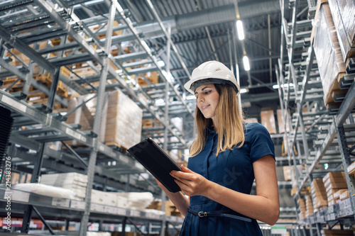 Beautiful young woman worker of furniture store in shopping center. Girl looking for goods with a tablet is checking inventory levels in a warehouse. Logistics concept