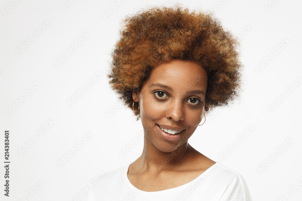 Closeup photo of young african american woman isolated on gray background with copyspace, dressed in white t shirt, turned to camera with one shoulder, smiling cheerfully Closeup photo of young african american woman isolated on gray background with copyspace, dressed in white t shirt, turned to camera with one shoulder, smiling cheerfully
