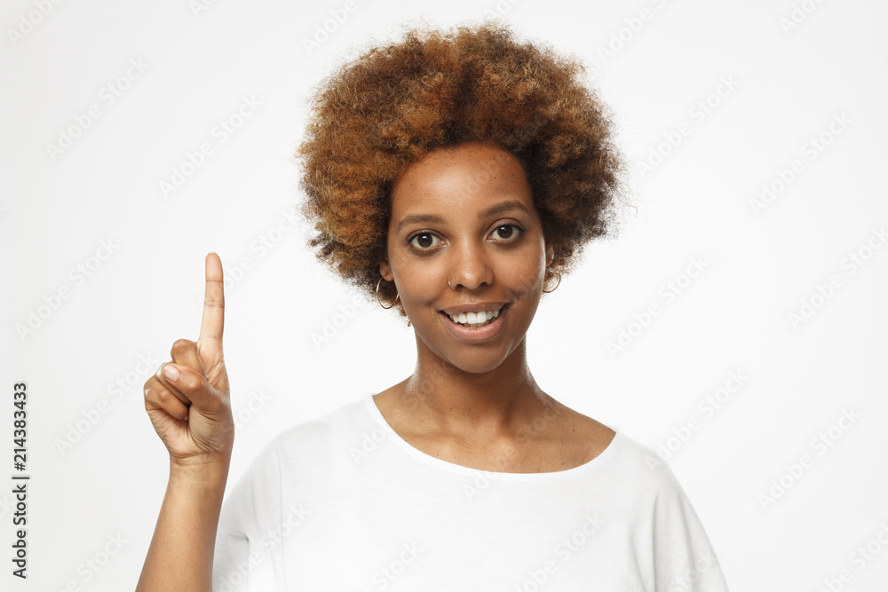 Attractive young african american woman in blank white t shirt, pointing up with his finger isolated on gray background Attractive young african american woman in blank white t shirt, pointing up with his finger isolated on gray background