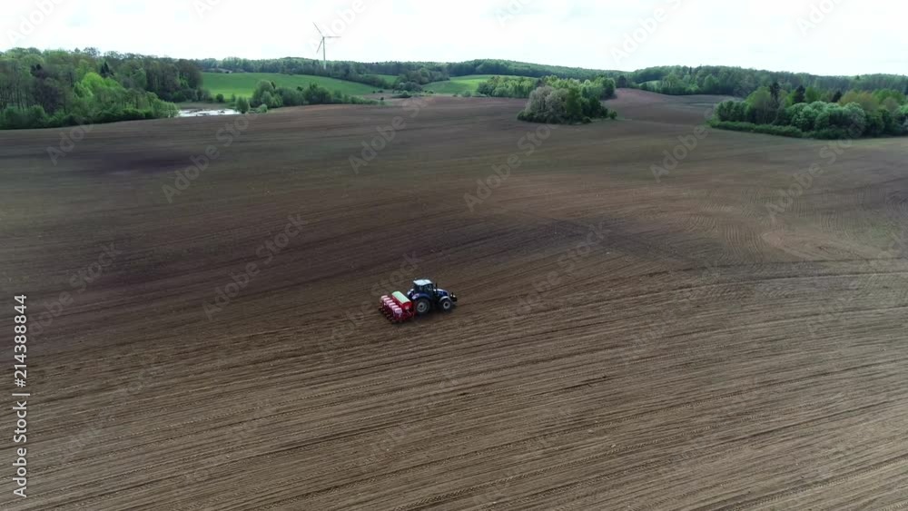Aerial view of a blue tractor seeding corn on a big farm field Aerial view of a blue tractor seeding corn on a big farm field