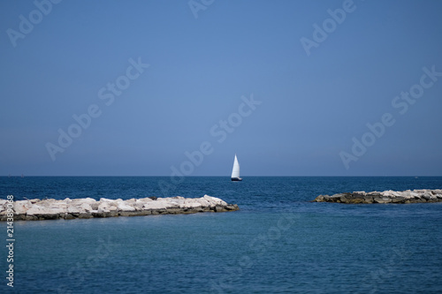 Yacht with a white sail against the background of the sea and the blue sky