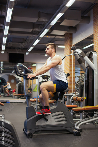 Fitness man on bicycle doing spinning at gym. Fit young man working out on gym bike.