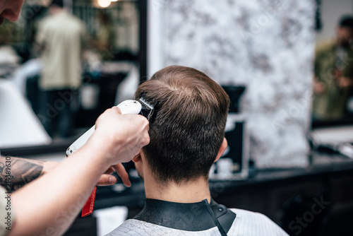 The hands of young barber making haircut to attractive man in barbershop