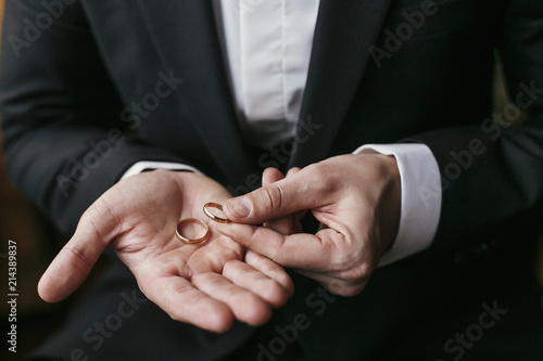 Wedding rings on palm hand. Groom in stylish suit holding golden wedding rings in hands, sitting in the room. marriage or divorce concept.
