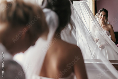 Foto bridesmaids and mother helping gorgeous bride getting ready for wedding