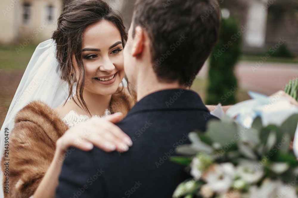 gorgeous bride with bouquet looking at stylish groom gently hugging in european city street in autumn time. happy wedding couple embracing. romantic sensual moment of newlyweds gorgeous bride with bouquet looking at stylish groom gently hugging in european city street in autumn time. happy wedding couple embracing. romantic sensual moment of newlyweds
