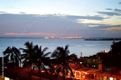 The sun sets in the Caribbean sea with palm trees at the foreground, in Cienfuegos Cuba