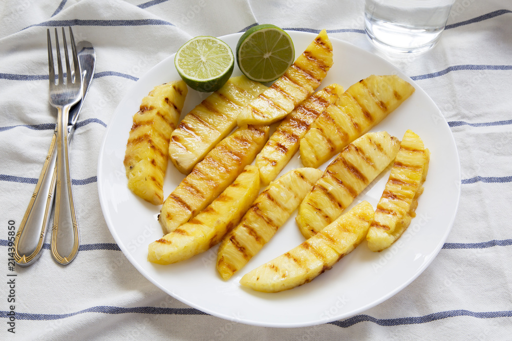 Grilled pineapple wedges with lime on white plate, side view. Summer food. Grilled pineapple wedges with lime on white plate, side view. Summer food.