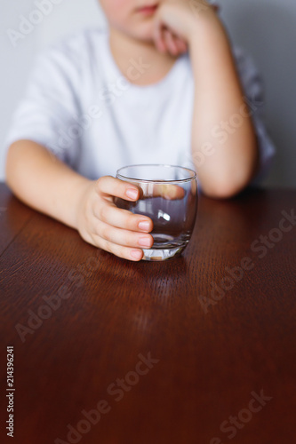 The boy is sitting at the table with an empty glass.