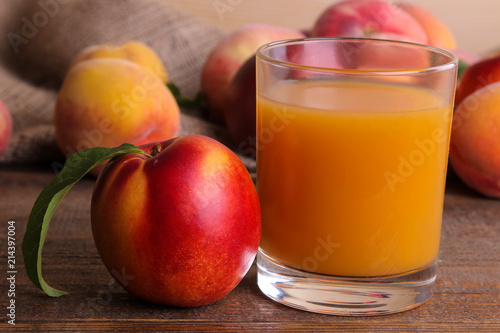 Peach juice in a glass next to a fresh peach closeup on a brown wooden background