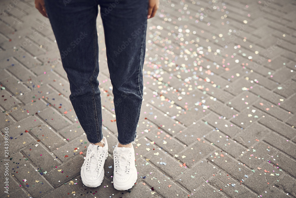 Close up girl legs wearing modern jeans and white trainers standing on bars with spangles outdoor Close up girl legs wearing modern jeans and white trainers standing on bars with spangles outdoor