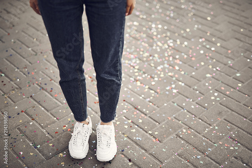 Close up girl legs wearing modern jeans and white trainers standing on bars with spangles outdoor