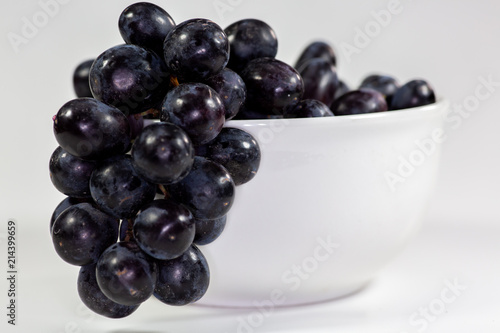 Black grapes in a deep white bowl on a white tale waiting to be eaten