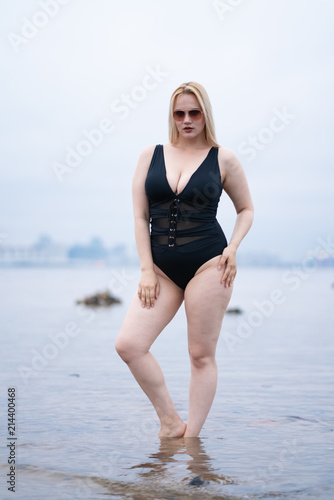 beautiful European plus size girl posing in black swimsuit on the beach alone